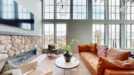 Located at 536 W Tremont Ave in Charlotte's South End neighborhood, this single-floor open-plan space makes a strong architectural statement from the moment you enter. Soaring double-height ceilings amplify the sense of volume, while expansive floor-to-ceiling steel-framed windows wrap the perimeter, flooding the interior with abundant natural light and offering sweeping views of the surrounding Charlotte cityscape.

The main living and lounge area centers around a dramatic river rock fireplace, clad in rounded natural stone that extends from floor to mid-wall, providing a warm, organic focal point. A wall-mounted flat-screen television above the fireplace adds a modern, functional element. Rich hardwood flooring runs throughout, complementing the sage-green walls and contributing to the space's warm yet contemporary aesthetic. A geometric pendant chandelier anchors the ceiling above the seating arrangement.

The dining area takes full advantage of the towering window wall, accommodating a substantial stone-top table surrounded by sleek chairs — an ideal setting for gatherings bathed in daylight and city views.

A built-in wood shelving unit near the entry serves as a curated display for an extensive collection of colorful agate crystal slices, introducing a unique and eye-catching decorative element that speaks to the space's distinctive character. Together, these features create a refined, design-forward environment well-suited for professional or hospitality use.