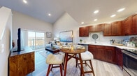 This two-story residence offers a well-designed layout spread across two floors, with the main level housing the primary living spaces and the upper level dedicated to bedrooms and a bathroom. The main floor features a striking open-concept kitchen, dining, and living area beneath soaring vaulted ceilings with recessed lighting, creating an airy, expansive atmosphere. The kitchen is outfitted with rich cherry wood cabinetry, stainless steel appliances including a range, microwave, dishwasher, and refrigerator, and light countertops that complement the warm wood tones. Light-toned hardwood-style flooring runs throughout the main level, enhancing the bright, welcoming feel. A sliding glass door in the living area opens to a balcony with open outdoor views. A carpeted staircase leads to the upper level, where the generously sized primary bedroom includes a walk-in closet. Two additional bedrooms feature plush carpeting and neutral tones. The shared bathroom includes a combined tub and shower, a cherry wood vanity, and light flooring consistent with the home's overall palette. A dedicated closet on the main level provides additional storage.