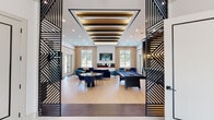 The Paragon clubhouse at 1008–1026 Larsen Road in Jackson, NJ is a thoughtfully designed, single-story amenity building that delivers a polished, upscale experience throughout. The grand lobby sets the tone immediately, featuring a curved reception desk set against a backlit geometric feature wall, bold circular pendant lighting, and gleaming white flooring that reflects the space's refined aesthetic.

The central lounge and social area is a showpiece, framed by dramatic geometric laser-cut metal screens and featuring a coffered ceiling with layered linear lighting. Light hardwood floors span the open space, which includes a dining area, a billiards table, and a plush seating cluster anchored by a wall-mounted TV and a modern multi-sided fireplace. Large windows fill the room with natural light and offer views of the outdoor surroundings.

A dedicated private theater provides a true cinematic experience, complete with tiered rows of blue and tan leather reclining seats, deep blue carpeting, acoustic wall panels, and soft sconce lighting for an immersive atmosphere. A popcorn machine adds a playful, hospitality-forward touch.

The Paragon Fitness center is well-equipped with treadmills, cycling bikes, free weights, and exercise balls, complemented by bold graphic wall striping and ample natural light. A separate conference room offers a round table, blue velvet seating, a wall-mounted display, and a stylish globe chandelier — ideal for private meetings. A large walk-in storage room with floor-to-ceiling shelving rounds out the facility's practical offerings.