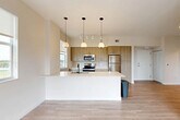 Located at 19277 NW 27th Ave in Miami Gardens, Florida, this well-appointed 2-bedroom, 1-bathroom residence offers a thoughtfully designed open-concept floor plan finished with light wood-tone flooring throughout. The combined living, dining, and kitchen area forms the heart of the home, bathed in natural light from multiple windows and sliding glass doors that open onto a private balcony with sweeping outdoor views of the surrounding greenery.

The kitchen is a standout feature, equipped with stainless steel appliances including a refrigerator, range, and microwave. Warm wood-grain cabinetry provides ample storage, while the large white quartz-style island with an undermount sink serves as both a prep space and a casual dining surface. Three stylish pendant lights hang above the island, complemented by track lighting above.

Both bedrooms are bright and comfortable, each featuring large windows that invite natural light and pleasant outdoor views. The primary bedroom offers a generous footprint with access to closet space. The bathroom includes a glass-enclosed walk-in shower, a wood-tone vanity with a white countertop, and tile flooring. A dedicated laundry area houses a stacked washer and dryer unit alongside built-in shelving for additional storage. The entrance hallway completes this clean, modern residence.