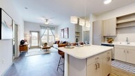 This thoughtfully designed 2-bedroom, 2-bathroom residence offers a seamless single-floor layout that maximizes comfort and functionality. The open-concept kitchen and living area serves as the heart of the home, featuring a central island with bar seating illuminated by stylish pendant lighting. The kitchen is outfitted with stainless steel appliances, light taupe cabinetry, and crisp white countertops, all set above durable wood-look flooring that extends throughout the main living areas. The living room is bright and welcoming, with a ceiling fan, large windows, and a glass door that opens directly onto a private balcony, filling the space with natural light and outdoor views. Both bedrooms are carpeted and well-proportioned, with large windows that bring in ample daylight. The primary bedroom offers generous space, while the second bedroom features tall ceilings and a serene, neutral palette. Each bedroom is complemented by its own closet. The two bathrooms are clean and modern — one features a soaking tub with tiled surround and built-in shelving, while the other includes a streamlined vanity with wood-look flooring. Together, the finishes and layout create a cohesive, contemporary living environment.