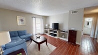 This single-floor residence offers a cohesive and functional layout highlighted by rich, dark wood-look tile flooring that flows consistently throughout the space, creating a warm and unified aesthetic.

The living area serves as the heart of the home, offering a comfortable and welcoming atmosphere. A large window dressed with light, grommet-top curtains allows natural light to fill the room, while a built-in shelving unit provides dedicated media and storage space. The textured ceiling adds a classic architectural character present throughout the home.

The kitchen is well-equipped with crisp white cabinetry, granite-style countertops, and a tasteful tile backsplash. Black appliances, including a refrigerator, electric range, and over-the-range microwave, provide a clean contrast to the bright cabinetry. A double-basin sink and a window above the counter further enhance the practicality of the space.

The bedroom is a restful retreat, complete with a ceiling fan, a closet, and neutral wall tones that promote a calm ambiance.

The bathroom features floor-to-ceiling tiled shower and tub surround with brushed nickel fixtures, including a grab bar for added accessibility, complemented by white cabinetry and matching countertops.

A central hallway connects all areas of the home efficiently, reinforcing the space's practical and comfortable single-floor design.