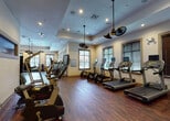 Located at 11338 SW 45th Pl in Miramar, FL, this fitness center offers a comprehensive, single-floor workout facility designed to accommodate a wide range of exercise needs. The space is finished with rich hardwood flooring throughout, contributing to a warm yet energetic atmosphere that encourages an active lifestyle.

The cardio zone is well-stocked with multiple treadmills — each equipped with individual digital display screens — alongside elliptical trainers and other aerobic machines, providing ample options for cardiovascular workouts. The strength training area features a variety of cable and resistance machines suited for both upper and lower body conditioning, complemented by a free weights section with a full dumbbell rack, benches, and wall-mounted mirrors for form monitoring.

Additional equipment includes a climbing apparatus, exercise bikes, and stability balls, ensuring versatility for all fitness levels. A wall-mounted flat-screen television adds an entertainment element to the space.

Architecturally, the facility features tray ceilings with recessed lighting and distinctive vintage-style pendant ceiling fans that provide both ambiance and airflow. Multiple windows dressed with wooden blinds line the walls, allowing natural light to filter in while maintaining privacy. The overall design balances functionality with aesthetic appeal, making this fitness center an inviting and well-appointed space for daily training.