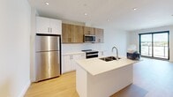 Located at 611 Davenport Rd in Waterloo, Ontario, this thoughtfully designed one-bedroom, one-bathroom unit offers a clean, modern aesthetic throughout its efficiently laid-out single floor. The open-concept kitchen serves as the heart of the space, showcasing a two-tone cabinetry design with warm wood-finish upper cabinets paired with crisp white lower cabinets. A large central island with a white quartz countertop and undermount double sink provides ample workspace and casual dining potential. Stainless steel appliances, including a full-size refrigerator, electric range, and built-in microwave, complete the contemporary kitchen setup. Light-toned hardwood flooring flows seamlessly throughout the main living areas and bedroom, lending warmth and continuity to the space. The bedroom is a calm, neutral retreat featuring a large window with a bold black frame that invites natural light and offers views of the surrounding neighbourhood. A sliding glass door visible from the living area leads to an outdoor space, enhancing the sense of openness. The bathroom is finished in clean white tones with a soaker tub and shower combination, complemented by sleek chrome fixtures. Recessed lighting throughout the unit adds a polished, modern touch to this well-appointed Waterloo residence.