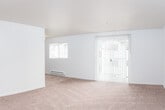 This single-floor residence offers a clean, functional layout designed for comfortable everyday living. The open living area is generously sized, finished with wall-to-wall carpet in a warm neutral tone and featuring a textured ceiling. Natural light fills the space through a side window and a set of sliding glass doors dressed with vertical blinds, which provide access to the outdoors. A baseboard heating system runs along the walls, ensuring efficient climate control throughout. The entryway, finished with hardwood-style flooring, leads seamlessly into the main living space and down a hallway connecting the rest of the unit. The galley-style kitchen is well-appointed with light wood cabinetry, ample counter space, and hardwood-style flooring. White appliances include a coil-top electric range with oven, a full-size refrigerator, and a dishwasher, complemented by overhead lighting and an exhaust hood above the range. Two bedrooms, each carpeted and bright, feature windows overlooking lush greenery and individual baseboard heaters. The bathroom is finished with hardwood-style flooring and includes a vanity, toilet, and towel bar, maintaining the unit's consistent, practical aesthetic throughout.