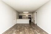 Located at 4946 Snapfinger Woods Dr in Decatur, GA, this single-floor unit offers a well-designed layout with consistent finishes throughout. The kitchen serves as a central highlight, featuring white shaker-style cabinetry, a mosaic tile backsplash in neutral tones, granite-style speckled countertops, and black appliances including a refrigerator, range, and dishwasher. A large peninsula island extends the counter space and provides a natural division between the kitchen and the open living area, making the space functional and ideal for entertaining. Rich, dark wood-style plank flooring runs throughout the unit, adding warmth and visual continuity across all rooms. The living area is bright and open, with multiple windows that allow natural light to filter in and offer views of the surrounding greenery. Neutral gray walls provide a clean, modern backdrop throughout. The bedrooms are well-proportioned, each with windows that bring in natural light. The bathroom is neatly appointed with a vanity featuring granite-style countertops, white cabinetry, a large mirror, and a shower-tub combination. A hallway connects the main living spaces to the bedrooms and bath, offering a practical and efficient floor plan overall.