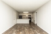 Located at 4946 Snapfinger Woods Dr in Decatur, GA, this single-floor unit offers a well-designed layout with consistent finishes throughout. The kitchen serves as a central highlight, featuring white shaker-style cabinetry, a mosaic tile backsplash in neutral tones, granite-style speckled countertops, and black appliances including a refrigerator, range, and dishwasher. A large peninsula island extends the counter space and provides a natural division between the kitchen and the open living area, making the space functional and ideal for entertaining. Rich, dark wood-style plank flooring runs throughout the unit, adding warmth and visual continuity across all rooms. The living area is bright and open, with multiple windows that allow natural light to filter in and offer views of the surrounding greenery. Neutral gray walls provide a clean, modern backdrop throughout. The bedrooms are well-proportioned, each with windows that bring in natural light. The bathroom is neatly appointed with a vanity featuring granite-style countertops, white cabinetry, a large mirror, and a shower-tub combination. A hallway connects the main living spaces to the bedrooms and bath, offering a practical and efficient floor plan overall.