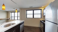 This 2-bedroom, 2-bathroom unit presents a thoughtfully designed single-floor layout that balances modern aesthetics with everyday functionality. The open-concept kitchen and living area serves as the heart of the home, featuring dark cabinetry contrasted by sleek white countertops and a central island that provides additional prep space and casual seating. Stainless steel appliances, including a gas range and built-in microwave, equip the kitchen for serious cooking, while a dishwasher adds convenience. A distinctive amber pendant light adds a warm accent to the space, complementing the track lighting overhead. Multiple large windows dressed with horizontal blinds flood the interior with natural light, creating a bright and airy atmosphere throughout. The polished dark concrete floors lend an industrial-modern character that ties the space together cohesively. The neutral wall tones provide a versatile backdrop that adapts easily to a variety of furnishing styles. With two well-appointed bedrooms and two full bathrooms, this unit offers comfortable accommodations suited for a range of lifestyles, from professionals to small families seeking a contemporary urban living experience.