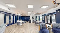 Located at 527 Herndon Square Ave in Atlanta, GA, this single-floor community space offers a thoughtfully designed and welcoming environment finished in a striking contemporary style. The open-plan layout is unified by bold navy blue accent walls, light wood-style flooring, and crisp white ceilings fitted with skylights and recessed lighting that flood the interior with natural brightness.

The main lounge area is generously proportioned, featuring multiple seating arrangements that cater to both social gatherings and quiet relaxation. Curved sofas, swivel accent chairs, and modular ottomans in neutral tones create an inviting atmosphere, while statement ring and sputnik-style pendant chandeliers add a modern, artistic flair. Large glass doors and windows frame views of the surrounding exterior, reinforcing the connection between indoor and outdoor spaces.

A dedicated work or meeting area includes a long communal desk with ergonomic seating, ideal for productivity, complemented by decorative wall art and ample natural light from exterior-facing windows.

The kitchen is well-appointed with wood-grain cabinetry, white countertops, a subway tile backsplash, stainless steel appliances including a full-size refrigerator and dishwasher, a built-in sink, and a skylight overhead. Open floating shelves provide additional display and storage space, completing a functional yet stylish culinary area suited for community use.