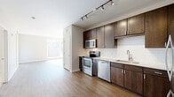 Located at 49 N Central Ave in the heart of Clayton, MO, this one-bedroom, one-bathroom unit on the third floor offers a well-designed layout that maximizes its efficient footprint. The open-concept kitchen and living area serves as the heart of the home, featuring rich dark-wood cabinetry that extends floor to ceiling, stainless steel appliances including a bottom-freezer refrigerator, electric range, microwave, and dishwasher, all complemented by a clean white tile backsplash and light countertops. Warm hardwood-style flooring runs throughout the main living areas, enhancing the bright, neutral palette. The living room receives generous natural light through large windows and a glass door that opens to an outdoor view of the Clayton cityscape, lending the space an airy, urban feel. The bedroom is a comfortable retreat finished with plush carpet, a large double-door closet for ample storage, and a sun-filled window overlooking the surrounding neighborhood. A hallway leads to the full bathroom, which features dark wood cabinetry, a wide vanity mirror, and coordinating finishes that tie together the unit's consistent design language. Clean lines, neutral tones, and quality finishes throughout make this a polished and functional urban residence.