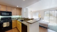 This single-floor residence offers a thoughtfully designed layout that balances comfort and functionality. The open-concept kitchen is a standout feature, equipped with warm maple cabinetry, granite countertops, black appliances including a gas range, built-in microwave, refrigerator, and dishwasher, all set over hardwood flooring. A peninsula with counter seating connects the kitchen seamlessly to the living area, which is bathed in natural light streaming through large sliding glass doors and vertical blinds that open to an outdoor view of lush greenery.

The living space flows naturally toward the entry, creating an inviting and connected atmosphere. Two carpeted bedrooms offer a quiet retreat, each featuring windows with blinds that frame views of the surrounding trees and allow abundant natural light. The bedrooms include walk-in or reach-in closets with built-in shelving for ample storage.

Both bathrooms are finished with granite-topped vanities, maple cabinetry, large mirrors, and tiled tub-shower combinations with sliding glass enclosures. Dark tile flooring anchors each bathroom with a clean, neutral aesthetic. Throughout the residence, a consistent palette of warm wood tones, neutral walls, and quality finishes creates a cohesive and comfortable living environment.
