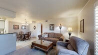 This single-floor residence offers a practical and comfortable layout across two bedrooms and three full bathrooms. The open-concept living area seamlessly connects the living room, dining room, and kitchen, creating a cohesive and functional communal space. The living room features plush carpeting, plantation shutters that allow for natural light control, and tile flooring near the entryway. The kitchen is equipped with white cabinetry, dark granite countertops, a tile backsplash, and a raised breakfast bar illuminated by pendant lighting and a skylight above, with direct sightlines into the dining area. A pantry and dedicated laundry room add everyday convenience. The primary bedroom is a comfortable retreat with warm-toned walls, crown molding, and carpeted floors. The second bedroom is similarly appointed with neutral tones and a closet. All three bathrooms feature tiled tub-shower combinations with curtains, tile flooring, and vanities with storage. Three closets throughout the home provide ample storage. The overall ambiance is warm and traditional, with classic wood furnishings, soft neutral color palettes, and practical finishes throughout.