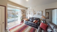 This single-floor residence offers a thoughtfully designed layout with a warm, cohesive aesthetic carried throughout each room. The living area serves as a central gathering space, anchored by a dark leather reclining sofa and accented by decorative wall art and iron sconces. A large sliding glass door floods the room with natural light and opens to a private balcony with outdoor views, creating a seamless indoor-outdoor connection.

The kitchen is well-appointed, featuring rich, dark wood cabinetry paired with dark granite-style countertops, light hardwood-style flooring, and a full suite of stainless steel appliances including a range, microwave, refrigerator, and dishwasher. A peninsula provides additional counter space and casual seating.

Two bedrooms offer comfortable, carpeted retreats. The primary bedroom accommodates a full furniture suite including a dresser, mirror, and nightstands, with windows providing natural light. The second bedroom is similarly sized and well-lit. Both bathrooms feature dark wood vanities, white countertops, large mirrors, and tub-shower combinations. One bathroom includes a tall built-in linen cabinet for additional storage. The overall ambiance is warm, inviting, and functionally organized.