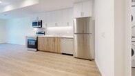 Located at 97 Milford Ave in Waterloo, Ontario, this thoughtfully designed 2-bedroom, 1-bathroom unit offers a clean, contemporary aesthetic throughout. Light-toned hardwood flooring runs seamlessly across the entire space, complementing the crisp white walls and creating a bright, cohesive feel.

The open-concept kitchen and living area forms the heart of the unit. The kitchen is well-appointed with two-tone cabinetry — white upper cabinets paired with natural wood lower cabinets — set against a white tile backsplash and light countertops. A full suite of stainless steel appliances, including a refrigerator, electric range, over-the-range microwave, and dishwasher, provides modern convenience. The adjacent living area is filled with natural light from a large front-facing window, with a black-framed entry door adding a bold contrast to the otherwise neutral palette.

Both bedrooms are generously proportioned with clean white walls and the same warm hardwood flooring. The primary bedroom features sliding glass doors that open to a private balcony with outdoor views, while the second bedroom includes a built-in closet with double doors. The full bathroom is finished with large-format tile surrounding a soaker tub and shower, complemented by neutral tones throughout. A utility room and hallway complete the layout, ensuring practical functionality within this well-organized space.