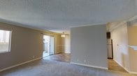 This single-floor residence offers a comfortable and functional layout with a seamlessly connected living and dining area. The living room is finished with plush wall-to-wall carpeting, neutral beige walls, and white crown molding that adds a clean, classic touch throughout. A textured popcorn ceiling contributes to the space's traditional character, while white baseboards provide a crisp contrast to the warm-toned walls.

Adjacent to the living room, the dining area features hardwood-style flooring and is anchored by a ceiling fan with a light fixture, offering both practical ventilation and ambient illumination. The transition between carpet and hard flooring clearly delineates the two functional zones while maintaining an open, airy feel between them.

A sliding glass door in the living area floods the space with natural light and provides direct access to an outdoor patio, offering views of the exterior surroundings and creating a welcoming indoor-outdoor connection. The overall ambiance of the space is calm and neutral, making it a versatile canvas well-suited for a variety of interior styles and furnishing preferences. The single-floor layout ensures easy accessibility and a cohesive flow throughout the home.
