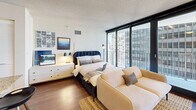 Located in the heart of Chicago's Streeterville neighborhood at 225 North Columbus Drive, this studio unit offers a smartly designed open floor plan that maximizes every square foot. Dark hardwood flooring runs throughout the main living area, anchoring a combined living and sleeping space bathed in natural light from floor-to-ceiling sliding glass doors. These doors open directly onto a curved private balcony, where sweeping views of the surrounding Chicago skyline create a striking urban backdrop.

The kitchen features stainless steel appliances, light wood cabinetry, and a breakfast bar with seating — an efficient and functional layout ideal for everyday living. Track lighting illuminates the living area, which flows seamlessly into the sleeping zone, separated by a pair of generous closets providing ample storage.

The bathroom is finished with neutral earth-tone tile surrounding a full soaking tub and shower combination, complemented by clean, classic fixtures. A dedicated laundry area adds everyday convenience, while a hallway entry with a large mirror creates a welcoming transition into the main space.

With its open-concept design, abundant natural light, private outdoor space, and prime downtown Chicago location, this studio delivers a functional and stylish urban living experience.