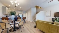 This thoughtfully designed multi-story home offers five bedrooms and four bathrooms across two active floors, delivering a comfortable and functional layout for everyday living. The main floor features an open-concept living, dining, and kitchen area unified by light wood-tone flooring and a neutral color palette. The kitchen is equipped with gray shaker-style cabinetry, stainless steel appliances including a French door refrigerator, a quartz-topped island with bar seating, and recessed lighting overhead. The adjacent dining area provides an intimate setting, while the living room benefits from abundant natural light through large windows and includes a ceiling fan. A staircase with clean white railings connects the floors. The upper floor hosts the bedrooms, including a primary suite with its own hallway leading to a walk-in closet and an ensuite bathroom featuring a glass-enclosed shower. Bedrooms are carpeted and receive generous natural light, with views of the surrounding landscape visible through wide windows. A carpeted hallway connects the upper-floor rooms efficiently. Additional features include a dedicated laundry area, a balcony, and four full bathrooms distributed throughout. The home's consistent modern aesthetic, light finishes, and practical layout make it a versatile and welcoming residence.