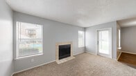 This well-appointed 2-bedroom, 2-bathroom single-floor residence offers a practical and comfortable layout across a compact, efficiently designed footprint. The living room serves as the heart of the home, featuring plush wall-to-wall carpeting, a textured ceiling, soft neutral gray walls, and a tile-surround wood-burning fireplace flanked by multiple windows that fill the space with natural light and offer views to the outdoors. A private entry door provides direct access to the living area. The kitchen is conveniently positioned and connects seamlessly to the living spaces. Both bedrooms are carpeted and well-lit by exterior windows, with the primary bedroom offering generous proportions relative to the overall floor plan. The secondary bedroom features warm hardwood-style flooring and a pendant light fixture. Each of the two bathrooms includes a full tub-and-shower combination — one highlighted by large white subway tiles with marble-accented niches, and the other with a clean white surround. Additional features include two closets for ample storage, a dedicated laundry area, and a hallway connecting the rooms. Throughout the home, consistent light gray walls and neutral finishes create a cohesive, move-in-ready atmosphere.