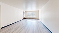 Located at 13751 32nd Ave NE in Seattle's Meadowbrook neighborhood, this one-bedroom, one-bathroom residence offers a well-organized single-floor layout with a thoughtful mix of comfort and functionality. The open-concept living and kitchen area forms the heart of the unit, featuring light gray laminate hardwood-style flooring that reflects natural light from the surrounding windows, giving the space an airy, bright feel. The kitchen is efficiently designed with dark walnut-toned cabinetry, light stone-finish countertops, a white electric range, refrigerator, and overhead lighting, making good use of the available space. The living area flows seamlessly from the kitchen and provides generous room for furnishings. The bedroom is carpeted for warmth and comfort, and includes access to a dedicated closet, with a total of four closets throughout the unit offering exceptional storage. A sliding glass door leads to a private patio, bringing in natural light and outdoor access. The full bathroom features a clean white tub-shower combination. Neutral wall tones, textured ceilings, and dark baseboards provide a cohesive and tidy aesthetic throughout. This unit is an ideal option for those seeking a practical and well-appointed home in a residential Seattle neighborhood.