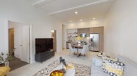 This thoughtfully designed single-floor residence offers a seamless open-concept layout that connects the living, dining, and kitchen areas into one cohesive and functional space. The living room is defined by soaring ceilings with decorative beam detailing, large windows dressed with sheer curtains that invite an abundance of natural light, and light-toned flooring that runs throughout. The kitchen features flat-front cabinetry in a warm wood finish, stainless steel appliances including a range, microwave, and French door refrigerator, a subway tile backsplash, and open shelving for added display and storage. A round dining table positioned between the kitchen and living area creates a natural flow ideal for everyday living and entertaining. The bedroom is a calm retreat with plush carpeting, a generous window with outdoor views, and direct access to a walk-in closet. The bathroom is finished with a wood-front vanity, a grey stone countertop, an undermount sink, and a full soaking tub with shower. Clean white walls, recessed lighting, and a consistent neutral palette give the entire space a modern, polished aesthetic throughout.