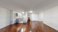 This 2-bedroom, 2-bathroom residence is laid out across a single floor, offering a practical and well-organized living environment. The space is immediately distinguished by its rich, warm parquet hardwood flooring, which flows consistently throughout the living areas, hallway, and bedrooms, lending the interior a classic yet timeless character.

The open living room is generously proportioned relative to the overall footprint, bathed in natural light from a large window that frames lush green outdoor views. A baseboard heating unit runs along the exterior wall, ensuring efficient climate control. The neutral white walls provide a clean, versatile backdrop throughout.

The kitchen has been thoughtfully updated with grey flat-front cabinetry featuring brushed stainless hardware, light granite countertops, and light-toned tile flooring — a modern contrast to the warmer tones found elsewhere. A full-size refrigerator and cooktop are included, making the space fully functional.

The two bedrooms are well-defined, each featuring the characteristic parquet flooring and white walls. The second bedroom benefits from its own large window with a pleasant outdoor view, while the primary bedroom, though compact, is efficiently sized. Two bathrooms serve the residence, adding convenience for occupants. A connecting hallway ties all areas together in a cohesive, easy-to-navigate layout.