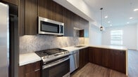 Located at 6606 Variel Ave in the Canoga Park neighborhood of Los Angeles, this modern single-floor residence showcases a thoughtfully designed interior with high-quality finishes throughout. The kitchen is a standout feature, outfitted with rich dark wood cabinetry extending to the ceiling, sleek white quartz countertops, and a striking stone-tile backsplash. A full suite of stainless steel GE appliances — including a gas range, over-the-range microwave, dishwasher, and french-door refrigerator — delivers both function and style. Pendant lighting adds a refined touch above the kitchen peninsula. The open living area features warm wood-toned luxury vinyl plank flooring and recessed lighting, with a large window allowing natural light to fill the space. The bedroom is finished with plush carpet flooring and includes a glass-paned door leading to a private outdoor area, with blinds providing added privacy. The bathroom is cleanly appointed with large-format tile flooring, a wood-finish vanity, an LED-backlit mirror, and a bathtub with shelving. A dedicated in-unit laundry closet with a stacked washer and dryer adds everyday convenience. The overall aesthetic is clean, contemporary, and move-in ready.