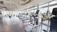 This expansive fitness facility in Durham, NC is thoughtfully designed to support a comprehensive workout experience within a bright, open single-floor layout. Floor-to-ceiling windows line the perimeter walls, flooding the space with abundant natural light and offering views of the surrounding outdoors, creating an energizing atmosphere for exercise. The high ceilings with exposed ductwork and pendant lighting contribute to an airy, industrial-modern aesthetic throughout.

The gym is generously equipped with a wide array of cardio machines, including rows of treadmills, ellipticals, stationary bikes, rowing machines, and spinning cycles, all arranged to take full advantage of the natural light and outdoor views. A dedicated strength training zone features cable machines, free weights, weight racks, benches, and multi-functional resistance equipment, providing options for both beginners and advanced users.

A standout feature is the bold, colorful geometric mural adorning one of the interior walls, adding a vibrant artistic focal point that energizes the space. Durable rubber flooring throughout ensures safety and comfort during workouts. Mirrors along key wall sections enhance the sense of openness and allow users to monitor their form. The overall ambiance is clean, modern, and motivating, making this facility a well-equipped destination for fitness in Durham.