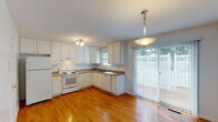 This three-floor space offers a practical and straightforward layout designed for comfortable everyday living. The kitchen is well-equipped, featuring white raised-panel cabinetry extending to the ceiling for generous storage, a full suite of white appliances including an electric range, dishwasher, and refrigerator, and neutral laminate countertops. Warm hardwood flooring runs throughout the kitchen, which also benefits from natural light through a window above the sink and a sliding glass door providing direct access to an outdoor area. The living spaces are carpeted and open in feel, with neutral white walls and sliding glass doors that bring in additional natural light and connect the interior to the outdoors. A staircase with a wood handrail connects the floors, accompanied by a hallway that transitions between hardwood and carpeted areas. The bathrooms include a half bath with a vanity and mirror, and a full bath featuring a tub-shower combination with tile flooring. The lower level contains a spacious attached garage with concrete block walls, a concrete floor, an automatic garage door opener, and an electrical panel, offering substantial storage or parking capacity.