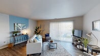 This single-floor residence offers a well-organized layout that balances comfort and functionality across its living spaces. The living room serves as the central gathering area, featuring wood-look flooring, a large sliding glass door dressed with vertical blinds, and a bold blue accent wall that adds a vibrant focal point. Natural light filters through the expansive glass door, which provides views of the outdoors and lends the space an open, airy feel.

Adjacent to the living room, the dining area continues the accent wall theme with a deep teal feature wall, creating a cohesive design connection between the two spaces. Wood-look flooring carries through, and the room comfortably accommodates a four-person dining set.

The kitchen is equipped with warm-toned wooden cabinetry, granite-style countertops, a stainless steel sink, and a black dishwasher, offering practical workspace and storage.

The bedroom is carpeted for added comfort and includes a window with natural light, providing ample space for a bed and a small desk or workspace.

The bathroom features a clean, neutral palette with a white vanity, framed mirror, and a shower-tub combination with wood-look tile flooring, completing this well-appointed unit.