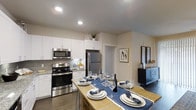 Located in Littleton, Colorado, this single-floor residence offers a thoughtfully designed open-concept layout that seamlessly connects the kitchen and dining areas. The kitchen is outfitted with stainless steel appliances, including a range, over-the-range microwave, and refrigerator, complemented by crisp white shaker-style cabinetry that extends to the upper walls for generous storage. A subway tile backsplash adds a clean, contemporary touch, while recessed lighting illuminates the space with a warm, even glow. The countertops provide ample workspace, and the open flow into the dining area makes the space ideal for both everyday living and entertaining. The dining area accommodates a full-sized table, as seen with the elegantly set wooden dining surface, reinforcing the home's welcoming atmosphere. Warm-toned hardwood-style flooring runs throughout, tying the spaces together cohesively. Neutral wall tones create a versatile backdrop that enhances the brightness of the interior. Additional rooms visible beyond the kitchen suggest a well-proportioned floor plan with thoughtful transitions between living spaces. Overall, this Littleton residence combines modern finishes with a functional, comfortable design suited for a variety of lifestyles.