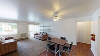 Located in East Lansing, Michigan, this single-floor unit offers a practical and straightforward layout designed for comfortable everyday living. The open living and dining area is a central highlight, combining hardwood flooring in the dining zone with carpeted lounge space. A ceiling fan overhead keeps the area comfortable, while vertical blinds on the sliding door and adjacent window allow for natural light and outdoor access. Built-in shelving along one wall provides convenient storage and display options.

The kitchen is efficiently arranged with white cabinetry above and below the counter, a stainless steel sink, and a coil-burner electric range — providing everything needed for daily meal preparation. The compact design makes good use of available space.

The bedrooms feature neutral carpeting and clean white walls, offering a calm and versatile environment. One bedroom includes a closet with direct access, while a second spacious room provides ample flexibility. Baseboard heating runs along the walls, ensuring warmth during Michigan winters.

The bathroom is notably well-appointed, featuring a double-sink vanity with a dark cabinet base and a wide mirror, alongside a separate shower-tub combination. The unit's clean, functional design makes it well-suited for individuals or small groups seeking practical accommodations in East Lansing.
