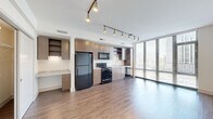 Located at 915 Thayer Ave in Silver Spring, Maryland, this efficiently designed single-floor unit offers a thoughtful open layout that maximizes every square foot. The combined kitchen and living area serves as the heart of the space, featuring warm hardwood-style flooring that flows seamlessly throughout. Floor-to-ceiling windows flood the living area with abundant natural light while framing views of the surrounding Silver Spring skyline, creating an open and airy atmosphere.

The kitchen is well-appointed with medium-toned wood cabinetry offering ample upper and lower storage, granite-style countertops, and a full suite of black stainless steel appliances including a refrigerator, electric range, over-the-range microwave, and dishwasher. A built-in desk area with matching cabinetry adds a functional workspace. Track lighting runs across the ceiling, providing directional illumination throughout both the kitchen and living areas.

The living area features clean white walls and a flexible open footprint, offering versatility in furniture arrangement. A hallway connects the main living space to the bathroom, which is finished with large-format tile flooring, a wood-framed vanity with granite-style countertop, a wall mirror, and a glass-enclosed walk-in shower. The overall design reflects a clean, contemporary aesthetic well-suited for modern urban living.