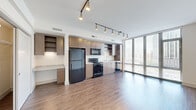 Located at 915 Thayer Ave in Silver Spring, Maryland, this efficiently designed single-floor unit offers a thoughtful open layout that maximizes every square foot. The combined kitchen and living area serves as the heart of the space, featuring warm hardwood-style flooring that flows seamlessly throughout. Floor-to-ceiling windows flood the living area with abundant natural light while framing views of the surrounding Silver Spring skyline, creating an open and airy atmosphere.

The kitchen is well-appointed with medium-toned wood cabinetry offering ample upper and lower storage, granite-style countertops, and a full suite of black stainless steel appliances including a refrigerator, electric range, over-the-range microwave, and dishwasher. A built-in desk area with matching cabinetry adds a functional workspace. Track lighting runs across the ceiling, providing directional illumination throughout both the kitchen and living areas.

The living area features clean white walls and a flexible open footprint, offering versatility in furniture arrangement. A hallway connects the main living space to the bathroom, which is finished with large-format tile flooring, a wood-framed vanity with granite-style countertop, a wall mirror, and a glass-enclosed walk-in shower. The overall design reflects a clean, contemporary aesthetic well-suited for modern urban living.