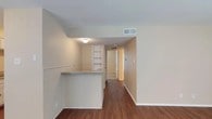 This single-floor residence offers a practical and comfortable layout with a cohesive neutral color palette throughout. The galley-style kitchen is well-appointed with white cabinetry featuring decorative hardware, granite-look countertops, a stainless sink, and white appliances including a refrigerator, range, and dishwasher. A pass-through breakfast bar with a stone-look countertop connects the kitchen to the main living area, creating an open, communicative flow between spaces. Rich hardwood-style flooring runs through the kitchen, living areas, and hallways, adding warmth and visual continuity. Built-in open shelving provides convenient display and storage space adjacent to the living area. The hallway leads to the bedrooms, each finished with plush carpet, ceiling fans with light fixtures, and blinds-covered windows that allow natural light while providing privacy. One bedroom includes a walk-in closet for ample storage. The two bathrooms feature hardwood-style flooring, tub and shower combinations with tile surrounds, and white cabinetry with paneled doors. The overall ambiance is clean, functional, and move-in ready, with a consistent warm-neutral tone that creates a welcoming atmosphere throughout.