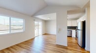 This single-floor residence is designed with a clean, contemporary aesthetic and a bright, open feel throughout. The living area is a standout space, featuring vaulted ceilings that add a sense of height and openness, warm hardwood-style flooring, and a fireplace framed by a shiplap-style surround. Natural light flows in through multiple windows fitted with blinds, and a sliding glass door provides direct access to an outdoor area.

The kitchen is well-appointed, offering white shaker-style cabinetry, light quartz countertops, and a striking dark tile backsplash with a linear pattern. Stainless steel appliances include a range, dishwasher, and refrigerator, and a window above the sink brings in additional natural light. The layout connects the kitchen visibly to the main living space via a half-wall partition.

The bedrooms feature plush neutral carpeting, ample natural light from windows, and closet storage. The bathroom continues the modern finishes seen throughout, with a white vanity, quartz countertop, coordinating tile accents, and hardwood-style flooring. Overall, the space presents a cohesive, move-in-ready interior with consistent finishes and a light, airy ambiance.