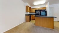 Located at 1413 Devon Ln in Harrisonburg, Virginia, this single-floor residence offers a well-organized layout with functional living spaces throughout. The kitchen is a standout area, featuring warm honey-toned wooden cabinetry, dark granite-style countertops, tile flooring, and a full suite of black appliances including a refrigerator, range, microwave, and dishwasher. A peninsula island provides additional counter space and a natural transition into the adjoining living area. The open-concept design allows the kitchen to flow seamlessly into the generously sized living space, which is finished with soft, neutral carpeting underfoot. Staircase railings with a wood-and-metal design add a subtle architectural detail to the main level. The bedrooms are comfortably sized with plush carpeting, neutral walls, and windows fitted with blinds that allow for natural light and outdoor views of the surrounding greenery. The bathroom is cleanly appointed with tile flooring, a wooden vanity with a light countertop, and a full tub-shower combination with crisp white surrounds. Throughout the residence, a consistent neutral color palette and clean finishes create a bright, move-in ready atmosphere well-suited to comfortable everyday living.