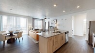 Located at 277 W 13490 S in Draper, Utah, this single-floor residence offers a well-designed, open-concept layout with modern finishes throughout. The kitchen serves as a central hub, featuring light wood cabinetry, granite countertops, a large island with an undermount sink, and a full suite of stainless steel appliances. Dark hardwood-style flooring flows seamlessly into the adjacent living and dining areas, which are bathed in natural light through expansive windows and a sliding glass door that opens to outdoor views. A ceiling fan and recessed lighting add both function and style to the living space. The primary bedroom is generously sized with plush carpeting, large windows, and direct access to a private en-suite bathroom. The en-suite includes a granite-topped vanity with light wood cabinetry, a large mirror, and dark hardwood-style flooring. A secondary bedroom, currently configured as a home office, features carpet flooring, bold teal drapery, and ample natural light. A second full bathroom includes a combined tub and shower, granite vanity, and clean, neutral finishes. A well-proportioned entryway with closet storage completes the layout. Throughout the residence, a consistent design palette of light wood tones, granite surfaces, and neutral walls creates a cohesive and contemporary ambiance.