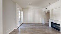 This well-appointed single-floor residence offers a clean, modern aesthetic with a neutral color palette and consistent wood-look flooring throughout the main living areas. The open living and dining space is a standout feature, filled with natural light streaming through multiple sets of French doors that open to an outdoor balcony area. A contemporary chandelier anchors the dining zone, while the generous layout allows for flexible furnishing arrangements.

The galley-style kitchen is thoughtfully designed with crisp white cabinetry extending to the ceiling, white quartz countertops, a stainless steel undermount sink, and updated appliances including a dishwasher and electric range. A large window above the sink brings in additional natural light, and tile flooring provides a practical surface underfoot.

The bedrooms are bright and tranquil, each featuring neutral walls, light wood-look flooring, and windows dressed with sheer curtains that diffuse soft natural light. The bathroom includes a white vanity with quartz countertop, a Hollywood-style light bar above a large mirror, and a full shower-tub combination. A long interior hallway connects the rooms, finished with the same wood-look flooring and a textured ceiling. Overall, the space presents a fresh, move-in-ready environment with a cohesive and understated design.
