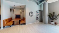 Located on Wardlaw Street in Greenville, South Carolina, The McClarin Podcast Studio is a purpose-built, single-floor space that seamlessly blends modern industrial design with warm, inviting interiors. The layout is anchored by a series of semi-private booth seating areas, each outfitted with rich cognac leather banquettes, solid wood tables, and Edison-style pendant lighting that casts a warm, focused glow. These booths are ideal for intimate recording sessions or collaborative meetings, with built-in display screens in select alcoves for content review or reference.

The main corridor connects the various zones of the studio, featuring soaring ceilings, exposed cylindrical columns, and light wood-look tile flooring that runs throughout, lending the space a clean and airy feel. Soft sage-green walls create a calming acoustic backdrop, complemented by curated artwork — including a standout framed Dalmatian print — that adds personality and visual interest.

A dedicated podcast recording room, accessible via a sliding barn door, offers a more enclosed environment with its own distinct design touches, including teal accent walls and focused task seating. Large street-facing windows at the front of the space introduce abundant natural light. Overhead, industrial ductwork and acoustic ceiling elements reinforce the studio's functional identity while enhancing its modern aesthetic.