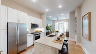This contemporary single-floor residence showcases a thoughtfully designed open-concept layout that seamlessly connects the kitchen, dining, and living areas. The kitchen is a standout feature, equipped with stainless steel appliances including a gas range, built-in microwave, and refrigerator, all complemented by crisp white shaker cabinetry, a classic subway tile backsplash, and light quartz countertops. A generously sized center island with a double undermount sink offers bar-style seating, making it ideal for casual dining and entertaining. Light wood-tone flooring flows throughout, adding warmth to the space. The living area benefits from large windows and a glass-paneled door that fills the room with natural light and provides outdoor views, with a ceiling fan adding comfort. The bedroom is a serene retreat, featuring wide windows with urban views, hardwood-style floors, and a bold accent wall that adds character and depth. The bathroom is well-appointed with a long vanity, ample cabinet storage, and tiled flooring, with a doorway leading directly to a walk-in closet, enhancing everyday convenience. Recessed lighting throughout ensures a bright, welcoming ambiance in every room.