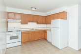 Located at 50620 Jefferson Ave in New Baltimore, Michigan, this single-floor unit offers a clean, straightforward layout designed for comfortable everyday living. The living area is generously proportioned, featuring warm beige carpeting and an abundance of natural light streaming through a large sliding glass door flanked by a side window, both dressed with vertical blinds. The sliding door opens to an outdoor space, providing a pleasant connection to the exterior. Baseboard heating runs along the walls throughout, ensuring efficient warmth. The kitchen is well-equipped with warm oak cabinetry extending to the upper walls for ample storage, light countertops, a gas range, a double-basin sink, and easy-to-maintain tile flooring. The bedrooms are spacious and carpeted, each offering natural light through windows with outdoor views and generous closet space with louvered doors. The full bathroom features tile flooring, a tiled shower and tub surround, a wide vanity with an oak cabinet base and light countertop, a large mirror, and a bright window fitted with vertical blinds. Throughout the unit, white walls and consistent finishes contribute to a bright, neutral, and move-in-ready ambiance suited to a variety of lifestyles.