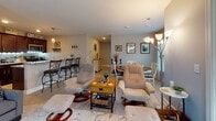 This thoughtfully designed single-floor residence offers a comfortable and functional layout with warm, neutral tones carried throughout. The open-concept living area features light wood-style flooring, large windows with decorative curtains that invite natural light, and a seamless flow into the dining space. The dining area accommodates a round wooden table with classic cream chairs, complemented by a glass wine rack and framed wall art. Adjacent to the dining room, the kitchen is outfitted with rich dark cabinetry, granite countertops, a tile backsplash with under-cabinet accent lighting, and a full suite of stainless steel appliances. A breakfast bar with bar seating adds additional dining convenience. The primary bedroom is a serene retreat with plush carpeting, ceiling fan, multiple windows, and ample dresser storage. A second bedroom offers equally comfortable carpeted flooring, natural light, and tasteful décor. Both bathrooms are well-finished; one features a dark wood vanity with granite countertops, a large framed mirror, and modern light fixtures, while the second includes a shower-tub combination. Throughout the residence, consistent warm-toned walls, recessed lighting, and quality flooring create a cohesive and inviting living environment.