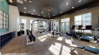 Located at 2200 Silver Crescent Dr in Charlotte, NC, this fitness center is a thoughtfully designed, single-floor facility built to support a wide range of workout routines. The space features a dramatic dark ceiling with recessed lighting that contrasts stylishly with white walls and a plaid-patterned floor, creating a modern and energetic atmosphere throughout.

The strength training area is a standout, anchored by a large multi-functional power rack system complete with barbells, a full set of adjustable dumbbells on tiered racks, medicine balls, kettlebells, resistance ropes, and TRX-style suspension trainers. A vibrant teal accent wall frames a large interior mirror, enhancing the sense of space and making it easy to monitor form during workouts.

A dedicated cardio zone is also present, featuring equipment such as treadmills and an elliptical machine. Geometric-patterned wallcovering adds a decorative touch to one section of the facility, while large windows on multiple walls flood the interior with abundant natural light and offer views of the surrounding community, including an outdoor pool area accessible through French doors. The open layout ensures ample floor space for stretching, functional training, and movement between stations.