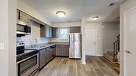 This two-story residence is thoughtfully laid out across two levels, offering a functional and updated interior throughout. The main level opens to a well-appointed kitchen featuring gray cabinetry, granite-style countertops, a white subway tile backsplash, and stainless steel appliances including a refrigerator and dishwasher. Wood-look plank flooring runs throughout the main living areas, complementing the neutral color palette. A spacious living area anchors the main floor, highlighted by a classic fireplace with a white mantel and a sliding glass door that invites natural light and provides access to the outdoors. Carpeted stairs with a metal railing connect the two floors. Upstairs, the bedrooms are finished with plush carpet and feature built-in closet storage, with ceiling fans providing additional comfort. A bathroom on the upper level is finished with large-format marble-look tile surrounding the tub and shower combination, paired with chrome fixtures for a clean, modern aesthetic. Textured ceilings are consistent throughout the home, adding a layer of visual interest to each room.