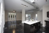 This single-floor loft-style space blends industrial design elements with modern finishes throughout. Polished concrete floors extend across the entire unit, reflecting light and adding a sleek, contemporary aesthetic. The open living area is defined by soaring ceilings with exposed metallic ductwork and track lighting, creating an urban, warehouse-inspired atmosphere. A ceiling fan and expansive French doors flood the space with natural light and provide direct access to an outdoor balcony with greenery views.

The kitchen is well-appointed with dark espresso cabinetry, light granite countertops, a subway tile backsplash, and a full suite of stainless steel appliances, including a refrigerator, electric range, and over-the-range microwave. A large granite-topped island serves as a central gathering point and additional prep space.

The bathroom features a granite vanity, glass-enclosed walk-in shower, and direct access to a spacious walk-in closet outfitted with wire shelving systems. A secondary bathroom includes a shower-tub combination with tile surround and overhead cabinetry. A dedicated laundry area houses a full-size washer and dryer with overhead shelving for added storage convenience.