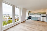 Located at 401 Union Ave SE in Olympia, Washington, this thoughtfully designed one-bedroom, one-bathroom unit offers a clean, modern aesthetic throughout. Light-toned hardwood flooring flows seamlessly across the entire space, enhancing its bright and airy feel.

The open-concept living and kitchen area is a standout feature, anchored by expansive floor-to-ceiling windows that flood the space with natural light and offer elevated views of the surrounding cityscape and tree canopy. The kitchen is well-appointed with sage-green cabinetry, stainless steel appliances including a range and dishwasher, and ample counter space, complemented by an additional window framing neighborhood views.

The bedroom is generously proportioned and wrapped with large corner windows that capture scenic views of Olympia, including glimpses of the Washington State Capitol dome. The room benefits from abundant natural light and connects to two closets for practical storage.

A hallway with clean white walls leads to the combined bathroom and laundry room. The bathroom features a tub-shower combination, a sage-green vanity with a white countertop, a large mirror, and a stacked washer and dryer conveniently integrated into the space.

The unit's contemporary design, abundant natural light, and elevated views make it a compelling residence in the heart of Olympia.