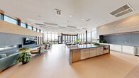 Located at 20 E Wilson St in downtown Madison, WI, this expansive single-floor amenity space offers a thoughtfully designed collection of areas for recreation, fitness, and social gatherings. The centerpiece lounge features a striking floor-to-ceiling stone fireplace flanked by a wall-mounted TV, complemented by contemporary seating and broad floor-to-ceiling windows that flood the space with natural light and frame sweeping city views. Adjacent to the lounge, a bright dining and social area showcases vibrant blue seating, a full kitchen bar, and large sliding glass doors opening onto an outdoor terrace with additional seating and panoramic views of the Madison skyline. The well-appointed fitness center is divided into two distinct zones: a cardio and cycling room with high clerestory windows providing natural light, and a strength training area equipped with free weights, a squat rack, and functional training equipment, all set on durable rubberized flooring with bold blue accent walls. A dedicated game room enclosed in glass features a billiard table and a wall-mounted TV, offering a casual retreat. Outdoor terraces include a landscaped courtyard with greenery and a turf area with railing-enclosed open-air space, both offering views of the surrounding urban environment. The hallway connecting these spaces maintains a clean, modern aesthetic throughout.