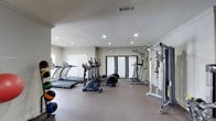 This fitness center offers a comprehensive workout environment designed to support a wide range of exercise routines. The space is outfitted with multiple cardio machines, including treadmills and elliptical trainers, providing ample options for aerobic training. A multi-function cable and weight machine anchors the strength training area, complemented by a selection of medicine balls and free weights neatly arranged along the wall. The flooring features durable, speckled rubberized material well-suited for high-traffic gym use, offering both traction and comfort underfoot. Recessed lighting throughout the ceiling ensures the space is well-lit, while a textured ceiling adds a finished look to the room. Neutral-toned walls contribute to a clean, focused atmosphere. Windows along one wall allow for natural light, enhancing the overall brightness of the space. An emergency exit door with clearly marked signage is conveniently located for safety. The layout is thoughtfully organized, allowing for comfortable movement between equipment. Crown molding along the upper walls adds a subtle architectural detail, lending the facility a polished appearance. Overall, this fitness center is a functional and well-maintained space suitable for a full-body workout regimen.