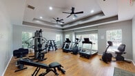 This fitness center in Jackson, Tennessee is a thoughtfully designed, single-floor facility that balances functional workout space with polished architectural details. The room is anchored by a distinctive tray ceiling fitted with recessed lighting and dual ceiling fans, creating a comfortable, well-ventilated environment during workouts. Warm hardwood flooring runs throughout, lending an inviting aesthetic that sets this space apart from a typical gym setting.

Natural light streams in through multiple windows fitted with horizontal blinds along multiple walls, offering views of the surrounding greenery and keeping the space bright and open. The neutral gray wall palette complements the overall modern design.

The fitness floor is well-appointed with a varied selection of equipment to support diverse workout routines. A multi-station cable and weight machine anchors the strength training area, accompanied by a freestanding dumbbell rack with a full range of weights. Cardio options include treadmills, an elliptical, and a Bodycraft rowing machine, providing a comprehensive range of aerobic training tools. An adjustable workout bench adds further versatility for strength exercises.

A dedicated open area provides ample room for stretching or floor-based workouts, and a separate entry door with a windowed panel allows for easy access. The facility is equipped with safety features including clearly marked exit signage and fire alarm systems throughout.