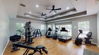 This fitness center in Jackson, Tennessee is a thoughtfully designed, single-floor facility that balances functional workout space with polished architectural details. The room is anchored by a distinctive tray ceiling fitted with recessed lighting and dual ceiling fans, creating a comfortable, well-ventilated environment during workouts. Warm hardwood flooring runs throughout, lending an inviting aesthetic that sets this space apart from a typical gym setting.

Natural light streams in through multiple windows fitted with horizontal blinds along multiple walls, offering views of the surrounding greenery and keeping the space bright and open. The neutral gray wall palette complements the overall modern design.

The fitness floor is well-appointed with a varied selection of equipment to support diverse workout routines. A multi-station cable and weight machine anchors the strength training area, accompanied by a freestanding dumbbell rack with a full range of weights. Cardio options include treadmills, an elliptical, and a Bodycraft rowing machine, providing a comprehensive range of aerobic training tools. An adjustable workout bench adds further versatility for strength exercises.

A dedicated open area provides ample room for stretching or floor-based workouts, and a separate entry door with a windowed panel allows for easy access. The facility is equipped with safety features including clearly marked exit signage and fire alarm systems throughout.